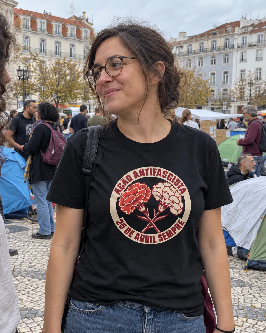 Pessoa a vestir a T-shirt Ação Antifascista em preto, no Rossio, entre as tendas da acampada
